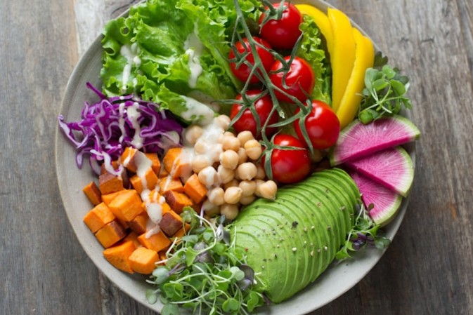Colourful salad bowl with avocado, chickpeas, roasted sweet potato, and fresh vegetables on a wooden table