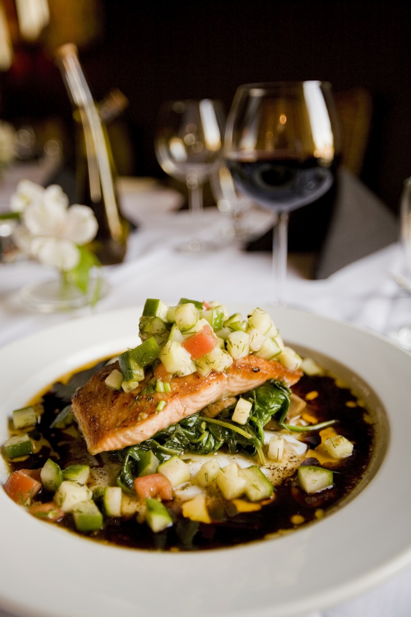 Pan-seared salmon on sautéed spinach with fresh cucumber and tomato salsa on a white plate